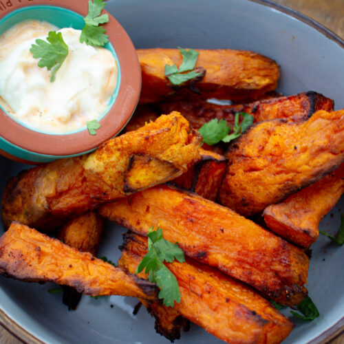 picture of crispy sweet potatos in a greeny/blue bowl with a side of dipping sauce. It is sprinkled with corriander