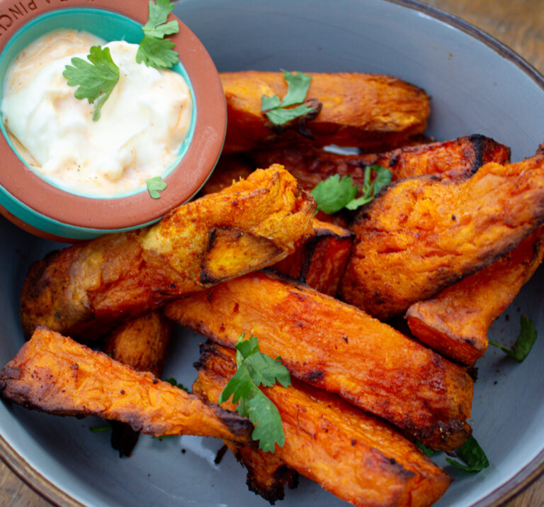 picture of crispy sweet potatos in a greeny/blue bowl with a side of dipping sauce. It is sprinkled with corriander
